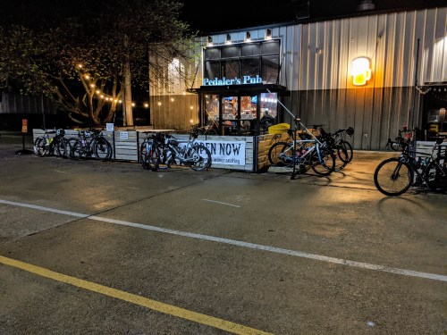 Bicycles parked outside Pedaler's Pub at night, with warm lights and a sign indicating it's open.