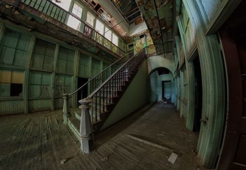 Abandoned interior of a building with a staircase, peeling paint, and green walls, creating a haunting atmosphere.