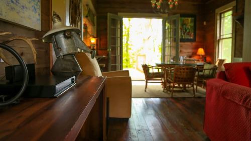 Cozy interior of a rustic room with wooden furniture, a table, and open doors leading to a lush outdoor view.