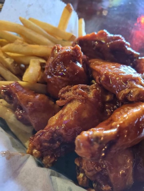 A plate of crispy chicken wings coated in sauce, served with a side of golden French fries.