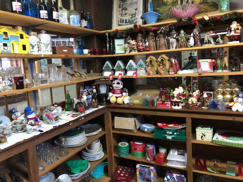 A cozy display of various collectibles, including figurines, glassware, and holiday decorations on wooden shelves.