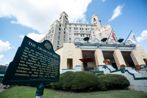 Historic Arlington Hotel with a plaque in the foreground, showcasing its architecture and surrounding greenery.