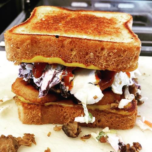 A stacked sandwich with toasted bread, filled with fried items, coleslaw, and sauces, resting on a cutting board.