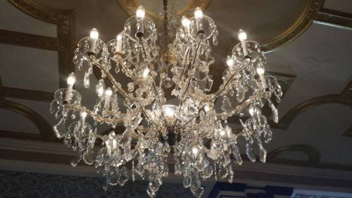 A large, ornate chandelier with multiple arms and sparkling crystals, illuminated by bright lights.
