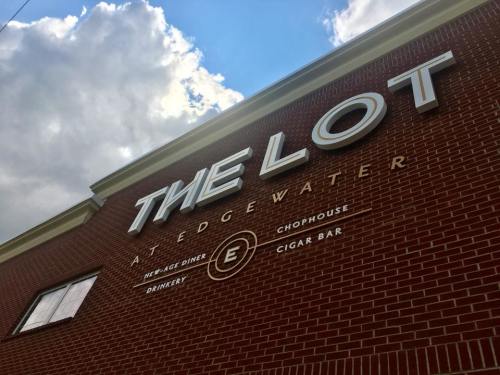 Sign for "The Lot at Edgewater" featuring a diner, chophouse, and cigar bar against a cloudy sky.