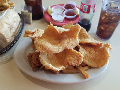 A plate of crispy fried fish served with fries, a basket of bread, and drinks on a table.
