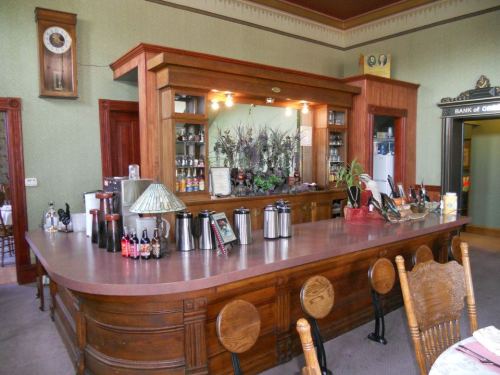 A wooden bar with a polished countertop, shelves of drinks, and decorative plants in a vintage-style interior.
