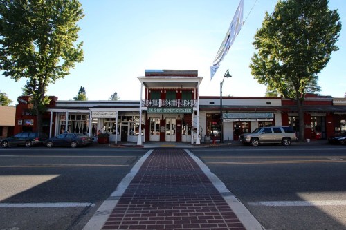 A street view of a charming small-town storefront with trees lining the sidewalk and a clear blue sky above.