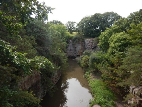 A serene river flows through a lush, green landscape with rocky cliffs and trees surrounding the water.