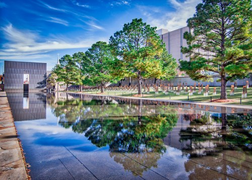 A serene memorial park with a reflective pool, surrounded by trees and a clear blue sky.