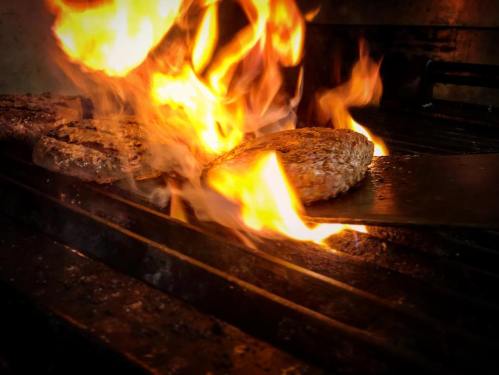 A burger patty sizzling on a grill, surrounded by flames and smoke.
