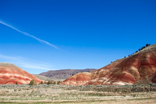 Colorful, layered hills under a clear blue sky, with sparse vegetation in the foreground.