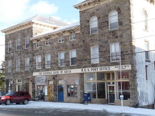 Historic stone building featuring a bank and post office, with snow on the ground and a red car parked outside.