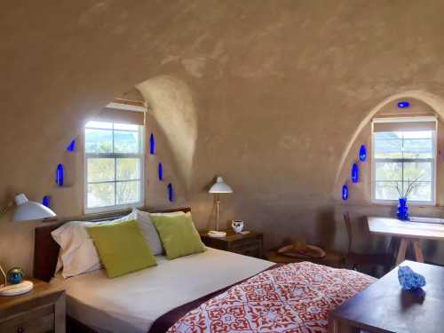 Cozy bedroom with a curved wall, large windows, and decorative blue glass accents, featuring a bed and wooden furniture.