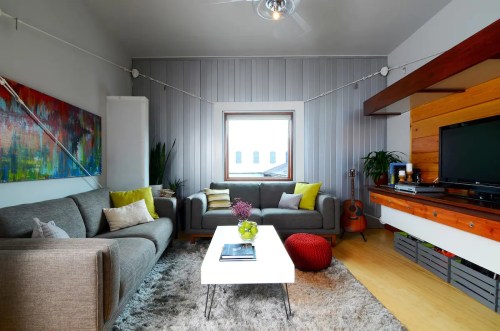 A modern living room with gray sofas, a white coffee table, colorful cushions, and a window with natural light.