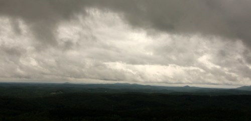 A panoramic view of a cloudy sky over rolling green hills and distant mountains.