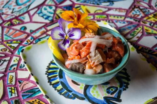 A colorful bowl of mixed seafood garnished with flowers and lemon, set on a vibrant, patterned table.