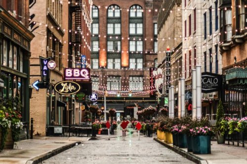 A charming street lined with restaurants and shops, adorned with string lights and colorful flower pots.