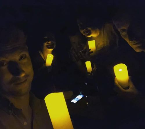 A group of people holding glowing yellow candles in a dimly lit setting, creating a warm, intimate atmosphere.