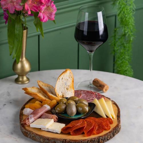 A charcuterie board with meats, cheeses, olives, dried fruits, bread, and a glass of red wine on a marble table.