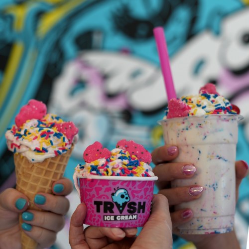 Three hands hold colorful ice cream treats: a cone, a cup with sprinkles, and a milkshake, all topped with pink candies.