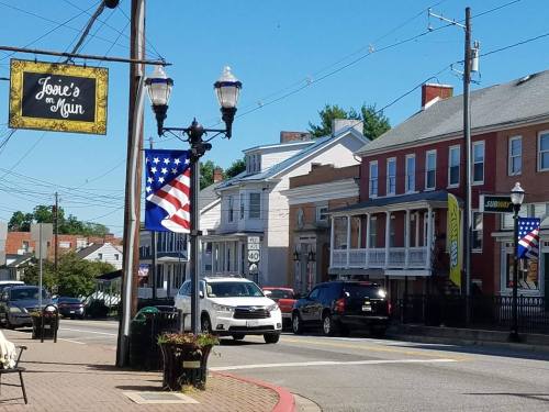A street view featuring buildings, American flags, and a sign for "Josie's on Main" on a sunny day.