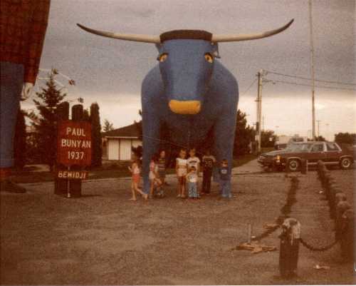 A group of children stands in front of a large blue bull statue, with a sign for Paul Bunyan in Bemidji, Minnesota.