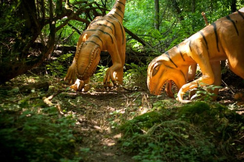 Two dinosaur sculptures with orange and black stripes are positioned in a lush, green forest setting.