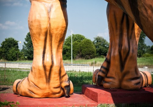 Close-up of large, painted dinosaur feet on a pedestal, set against a blue sky and green trees.