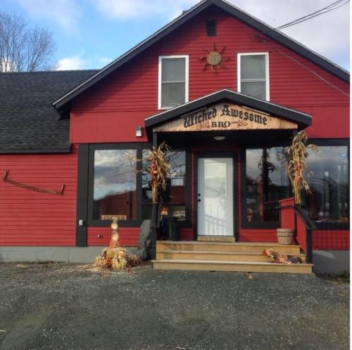 A red building with a sign reading "Wicked Awesome BBQ," decorated with corn stalks and autumn decor.
