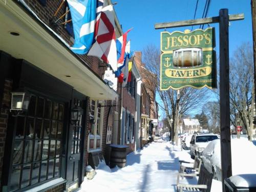 A snowy street scene featuring Jessop's Tavern sign and flags outside brick buildings.