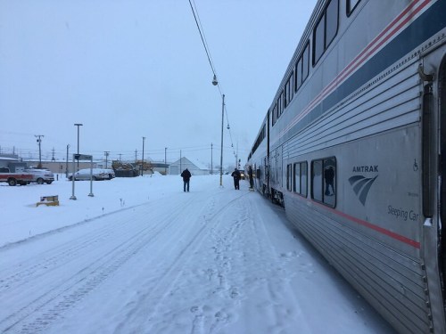 A snowy scene with an Amtrak train parked on a track, passengers disembarking in a winter landscape.