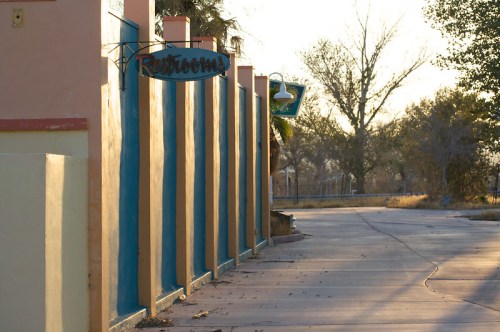 A pathway leading to restrooms, with colorful walls and trees in the background, illuminated by soft evening light.