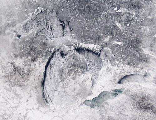 Aerial view of a snowy landscape featuring large lakes and intricate ice patterns.