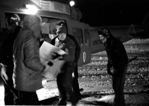 Black and white image of people unloading supplies from a helicopter at night in a snowy environment.