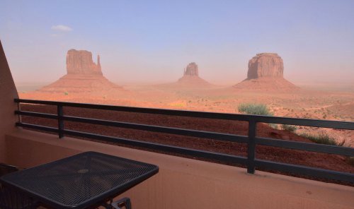 View of Monument Valley's iconic rock formations from a balcony, with a clear sky and reddish desert landscape.