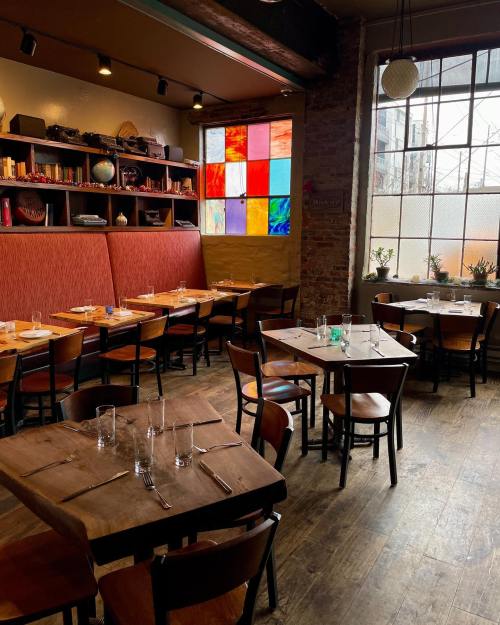 Cozy restaurant interior with wooden tables, chairs, and a colorful stained glass window. Warm, inviting atmosphere.