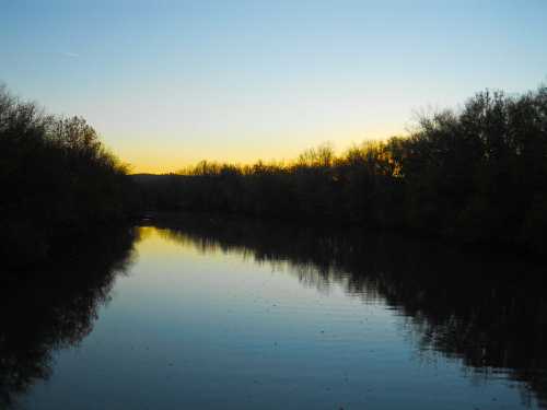 A tranquil river at sunset, reflecting the colorful sky and surrounded by trees.