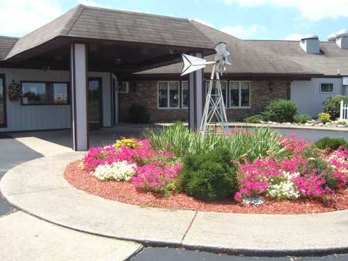 A landscaped entrance with colorful flowers, a circular path, and a decorative windmill in front of a building.