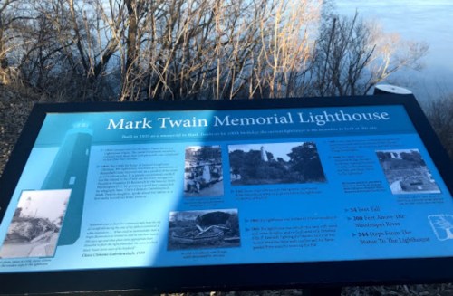 Sign for the Mark Twain Memorial Lighthouse, detailing its history and significance, with a view of the river in the background.