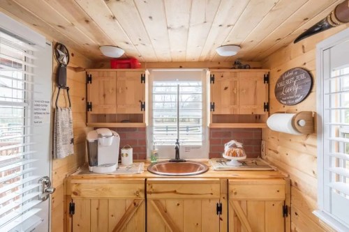 Cozy wooden kitchen with a copper sink, coffee maker, and a window, featuring rustic decor and warm lighting.