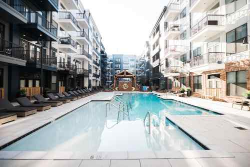 A modern apartment complex featuring a clear swimming pool surrounded by lounge chairs and balconies.