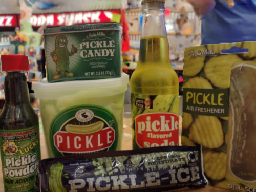 A collection of pickle-themed products, including candy, soda, air freshener, and pickle-flavored items.