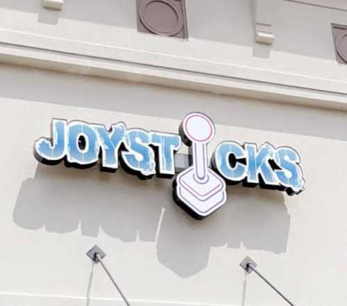 Sign for "Joysticks" featuring a joystick graphic, displayed on a light-colored building exterior.