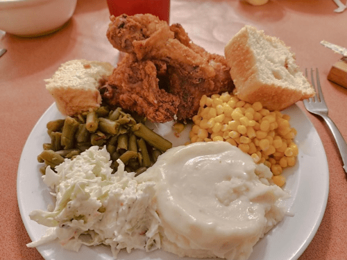 A plate of fried chicken, green beans, corn, coleslaw, mashed potatoes, and bread.