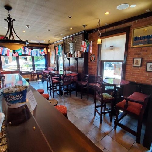 Cozy pub interior with wooden furniture, flags hanging, and a bar area, featuring a warm, inviting atmosphere.
