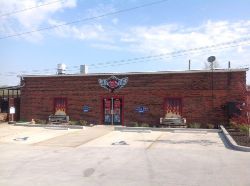 A brick building with a logo and flame designs on the windows, featuring accessible parking spaces in front.