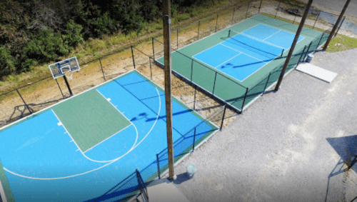 Aerial view of two basketball courts, one blue and one green, surrounded by a fence and trees in the background.