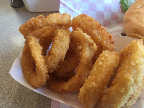A close-up of golden, crispy onion rings served in a paper tray.