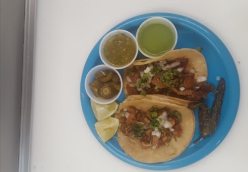 A blue plate with two tacos, lime wedges, jalapeños, and three small cups of salsa and green sauce.